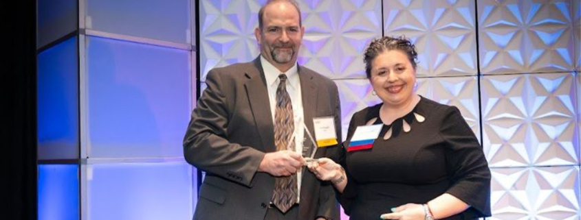 ATCS' Eric Mongelli accepting coprorate award on stage at an awards gala