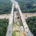Aerial view of a divided highway with ongoing construction in the center, surrounded by dense green forest and a river running parallel to the road.