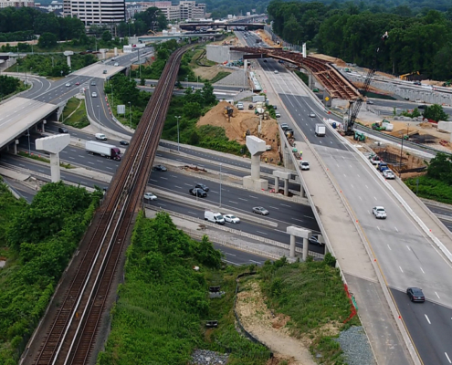 Aerial view of a highway interchange with multiple overpasses, a railway line, cars in motion, and ongoing road construction work.