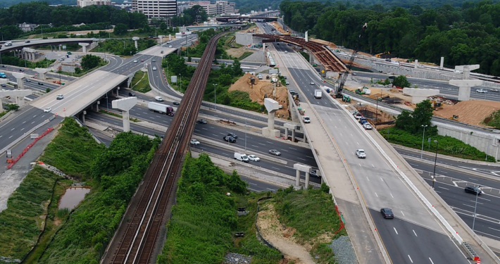 Aerial view of a highway interchange with multiple overpasses, a railway line, cars in motion, and ongoing road construction work.