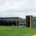 Modern gray community building with large windows, set on a green lawn under a cloudy sky. A stone accent marks the entrance.