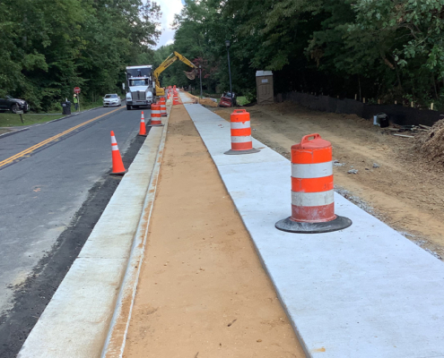 A sidewalk is under construction next to a road, with workers and equipment actively engaged in the building process.