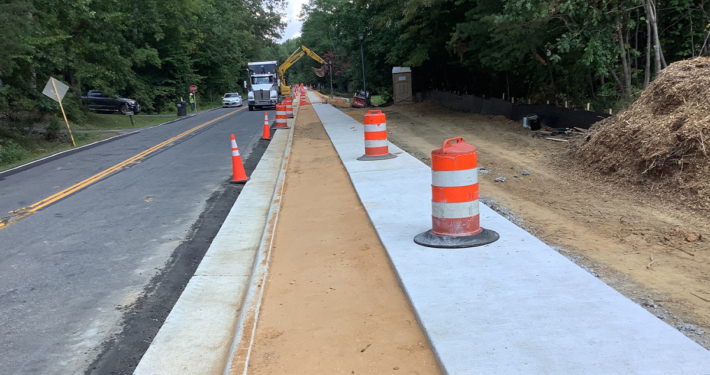 A sidewalk is under construction next to a road, with workers and equipment actively engaged in the building process.