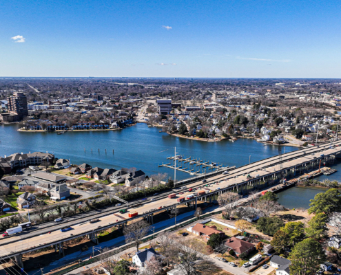 Aerial view of a city with a wide river, two bridges, and surrounding residential areas. The clear blue sky conveys a calm, sunny ambiance.