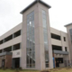 Large multi-story parking garage with tall glass-panel stair towers and open parking levels. Modern, urban design with a neutral tone under a cloudy sky.
