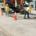 Construction workers actively working on a street in front of a building, using tools and machinery for repairs.