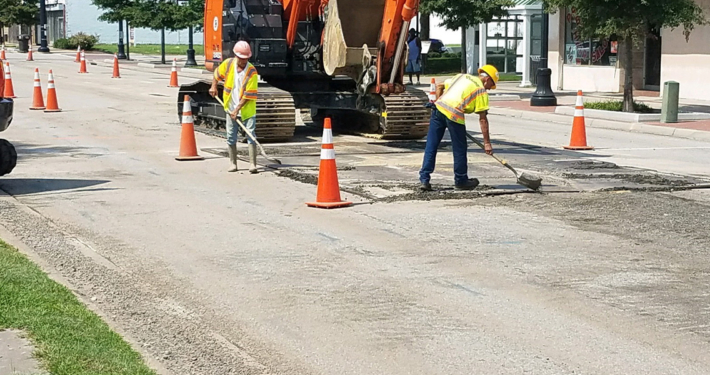 Construction workers actively working on a street in front of a building, using tools and machinery for repairs.