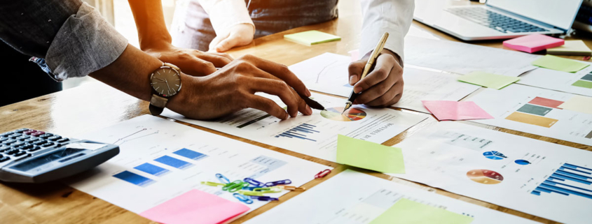 businessmen holding a pen pointing to paper graph on desk