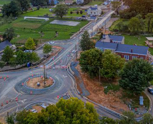 The sun sets over a town, casting warm hues on a roundabout surrounded by buildings and trees.