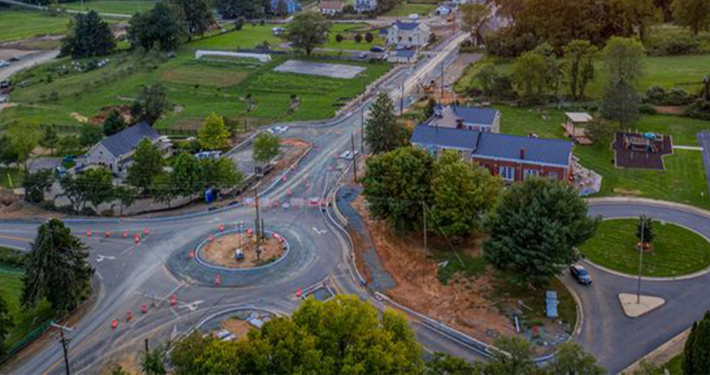 The sun sets over a town, casting warm hues on a roundabout surrounded by buildings and trees.