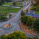 The sun sets over a town, casting warm hues on a roundabout surrounded by buildings and trees.