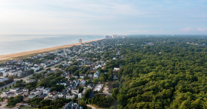 Aerial view of a beach town featuring houses, trees, and sandy shores under a clear blue sky